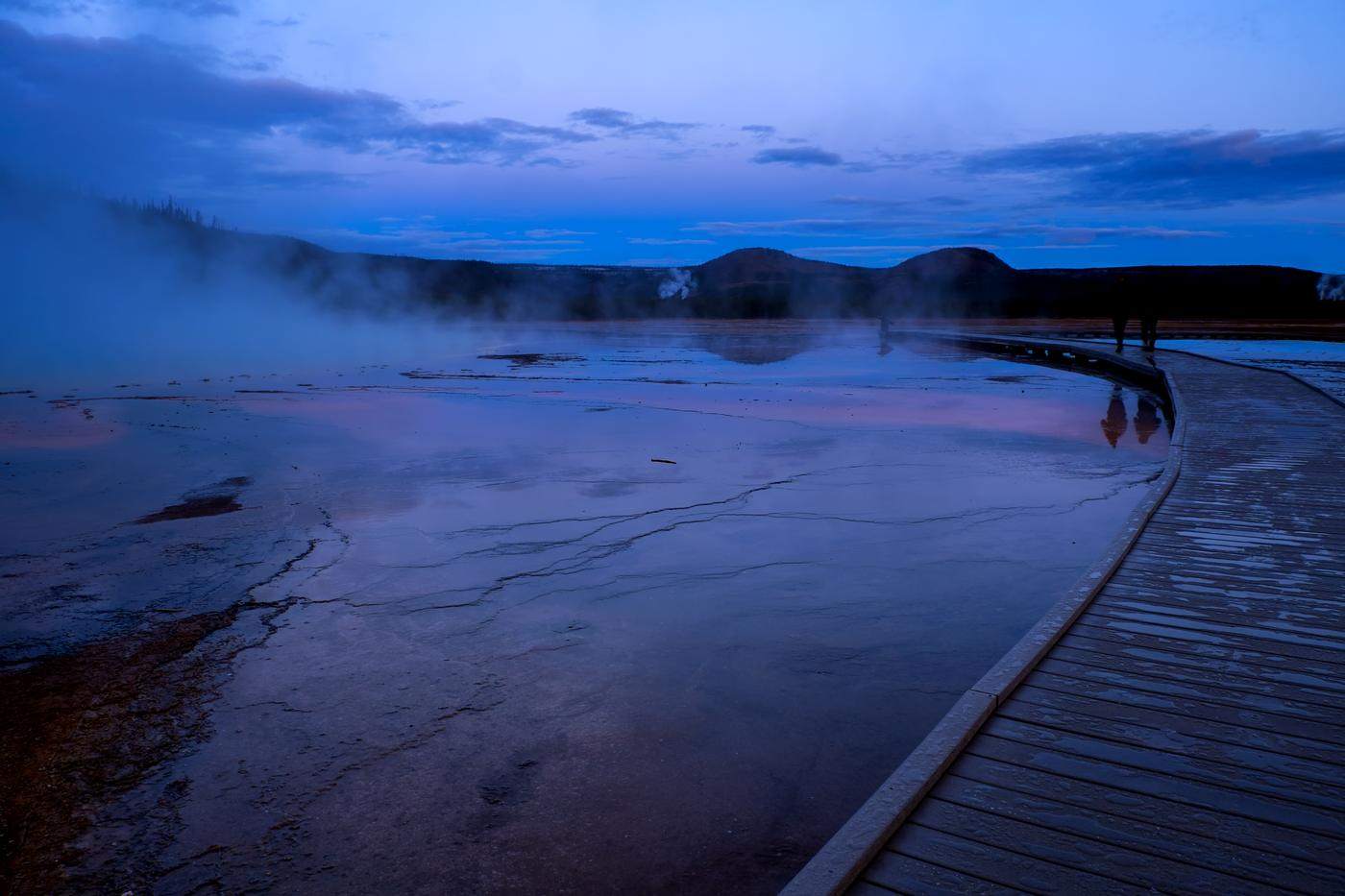 Blue-hour boardwalk curving across a steaming basin