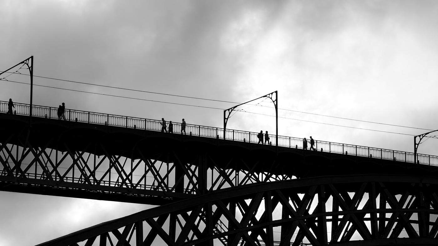 Pedestrians silhouetted crossing an iron arch bridge