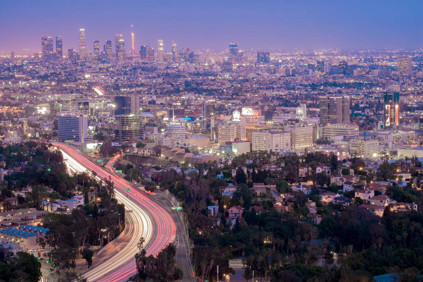 Freeway light trails curving toward a city skyline at dusk