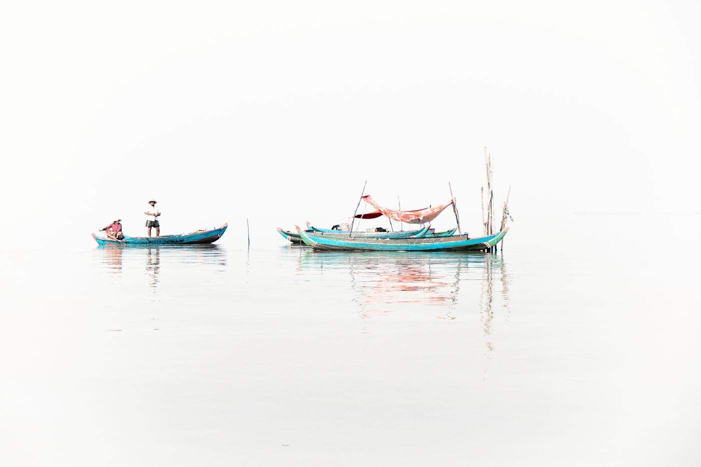 Turquoise fishing boats floating on pale, mirror-still water