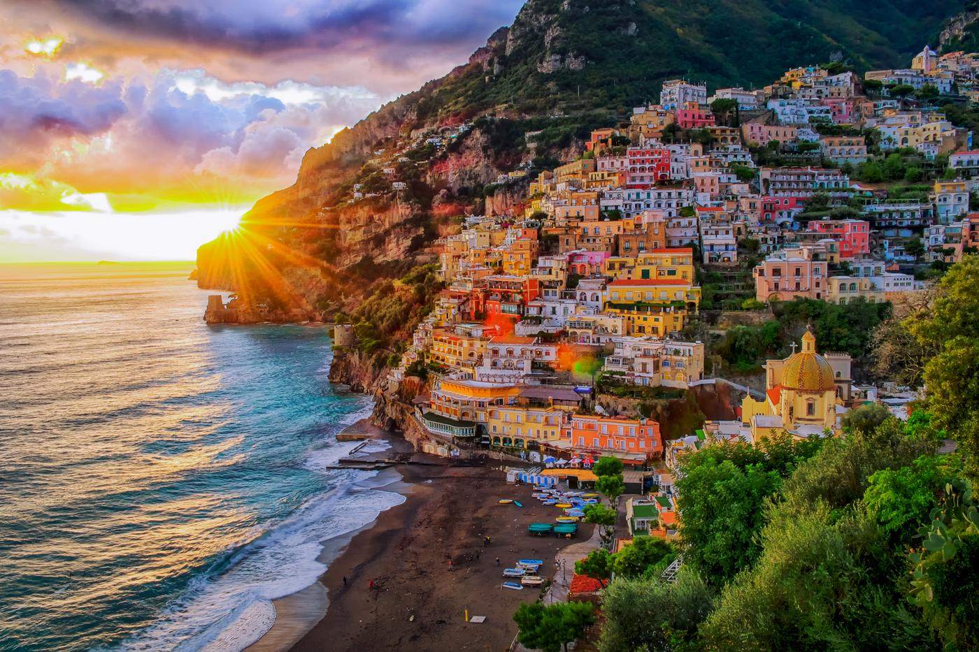 Positano at sunset, sun breaking over the cliffs above the colorful village and beach