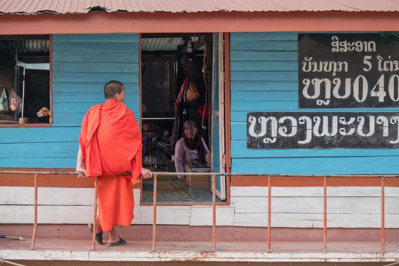 A monk in saffron robes standing before a blue wooden storefront
