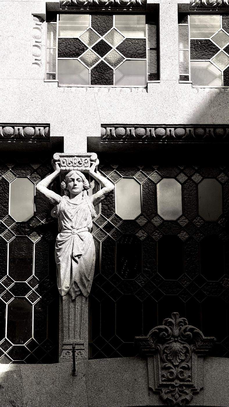 A carved stone caryatid against leaded glass windows